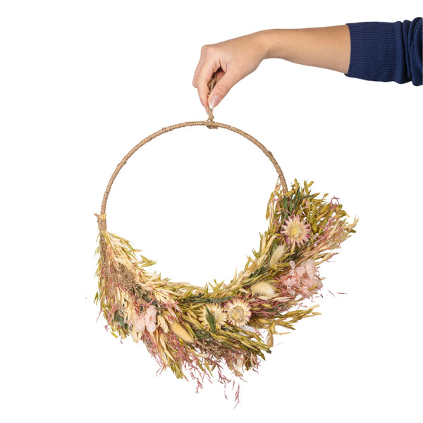 Hand holding a dried flower wreath against a white background