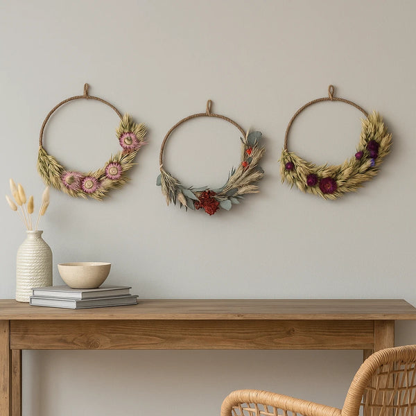 Three decorative wreaths on a wall above a wooden table with a vase and books.