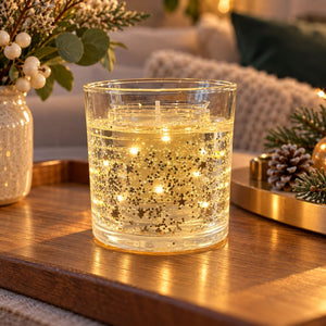 A clear glass candle jar with warm white star-shaped LED lights inside, sitting on a wooden tray in a cozy, decorated holiday setting.