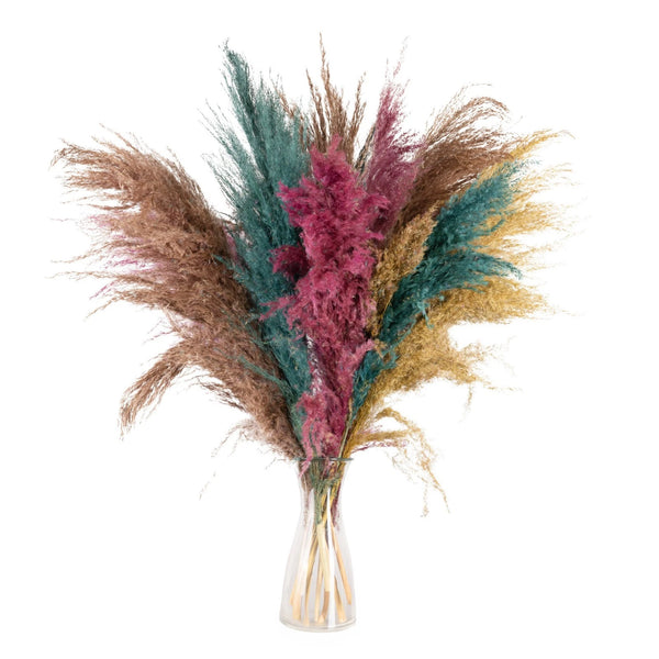 Bouquet of dried pampas grass with pink and green leaves in a clear vase on a white background