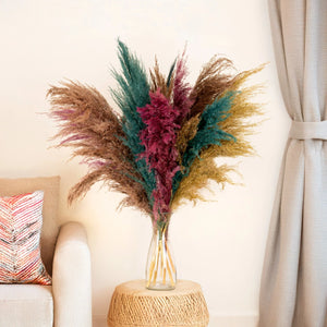 Vase with multicolored pampas grass on a side table next to a sofa with a pillow.