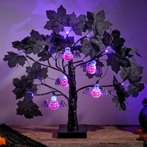 Black artificial grapevine tree light decoration with glowing purple LED fairy lights and hanging jack-o'-lantern bat ornaments, displayed on a wooden surface against a purple-lit background.