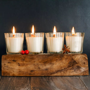 Four lit candles in glass holders on a wooden block with a dark background