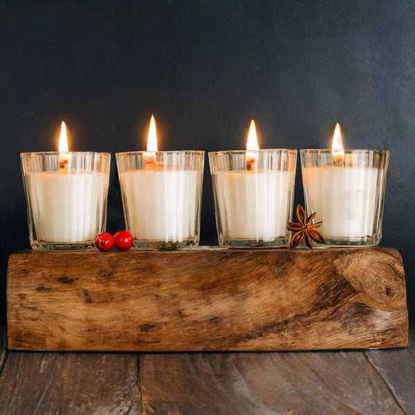 Four lit candles in glass holders on a wooden block with a dark background