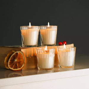 Four lit candles in glass holders on a reflective surface with a dark background