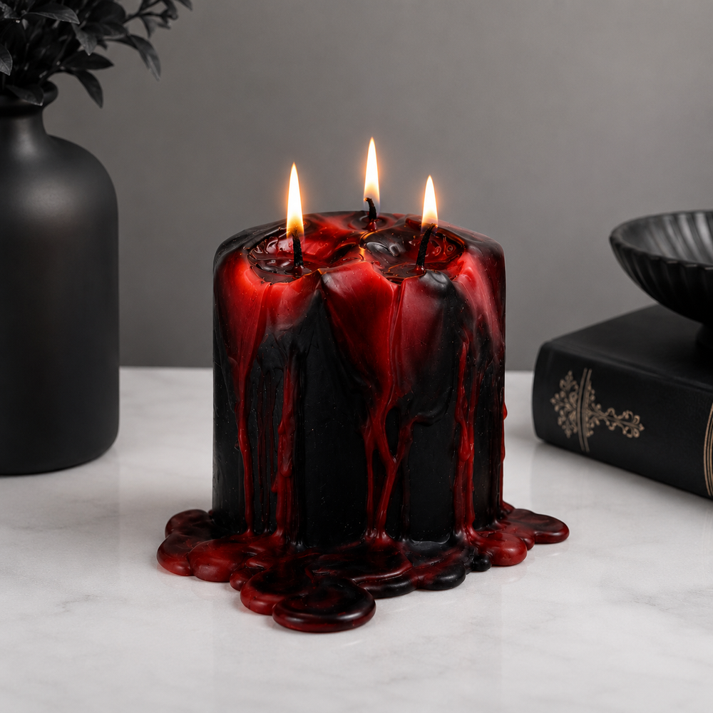 A black wax candle with dramatic red wax drips and three lit wicks, placed on a white marble surface with a dark vase and a black book in the background.