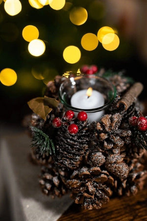 Decorative candle holder made of pine cones and berries with a blurred festive background.
