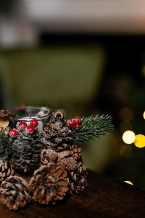 Decorative candle holder made of pine cones with berries and a small candle, set against a blurred festive background.