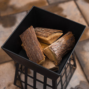 A black metal fire pit basket filled with cut firewood logs, shown from a top-down angle on a stone patio.