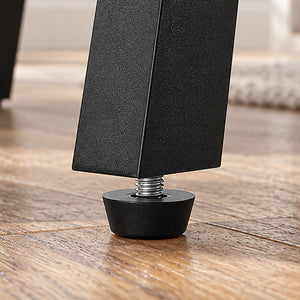 Close-up of a black adjustable furniture leg with a threaded metal bolt and round black rubber foot, standing on a wooden floor.