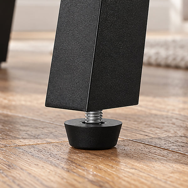 Close-up of a black adjustable furniture leg with a threaded metal bolt and round black rubber foot, standing on a wooden floor.