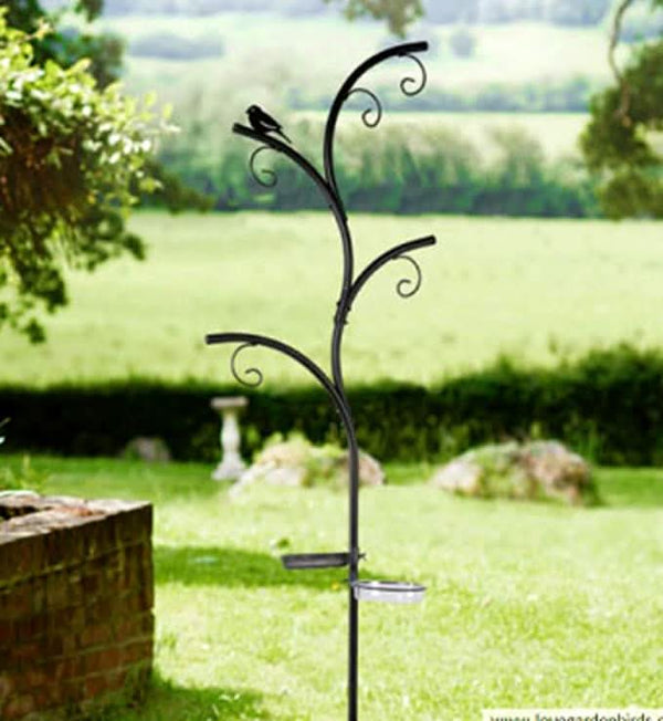 A metal wild bird feeder station designed to look like a tree set in a grassy garden area.