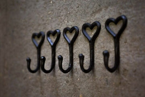 Five black heart-shaped hooks arranged in a row on a textured surface.