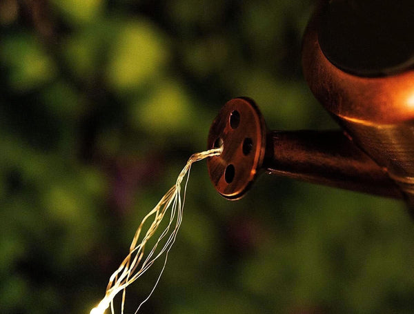 Decorative watering can hanging from a hooked garden stake
